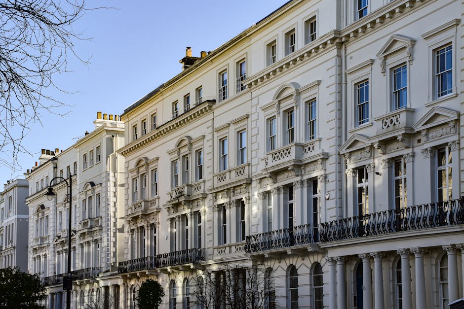 A white, multi-story residential building with ornate architectural details, including decorative window moldings and a curved balcony railing on the second floor, situated on Philbeach Gardens in Ear